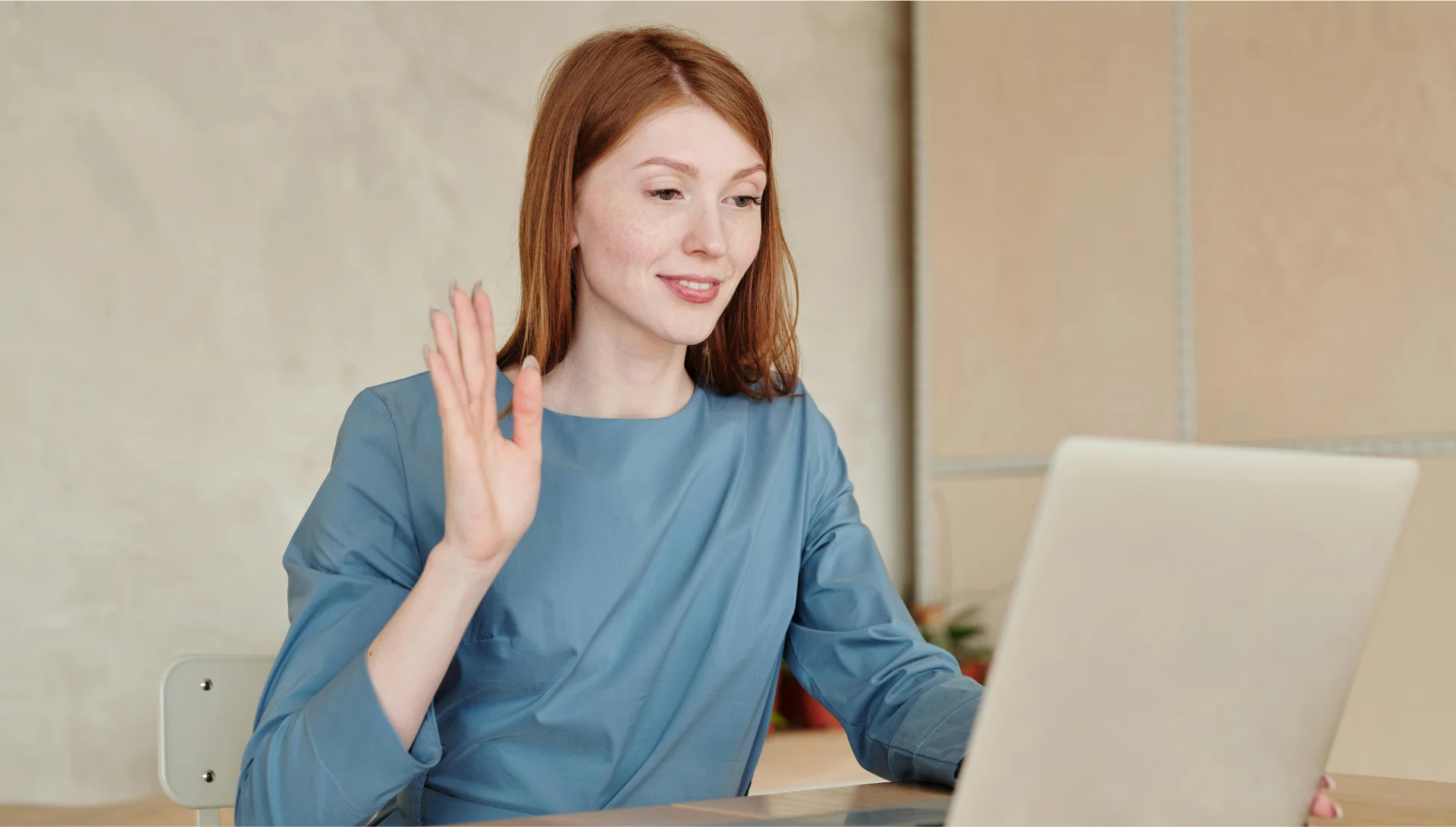 A woman waving during an online counselling session on her laptop