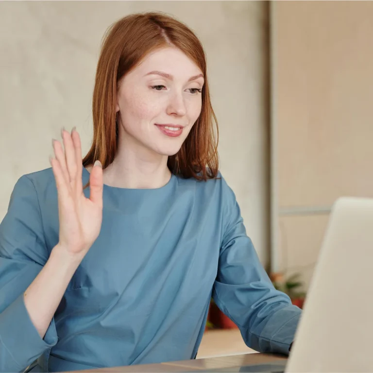 A woman waving during an online counselling session on her laptop